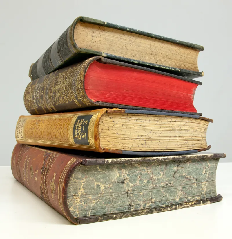 A stack of four old leather-bound books on a white surface.