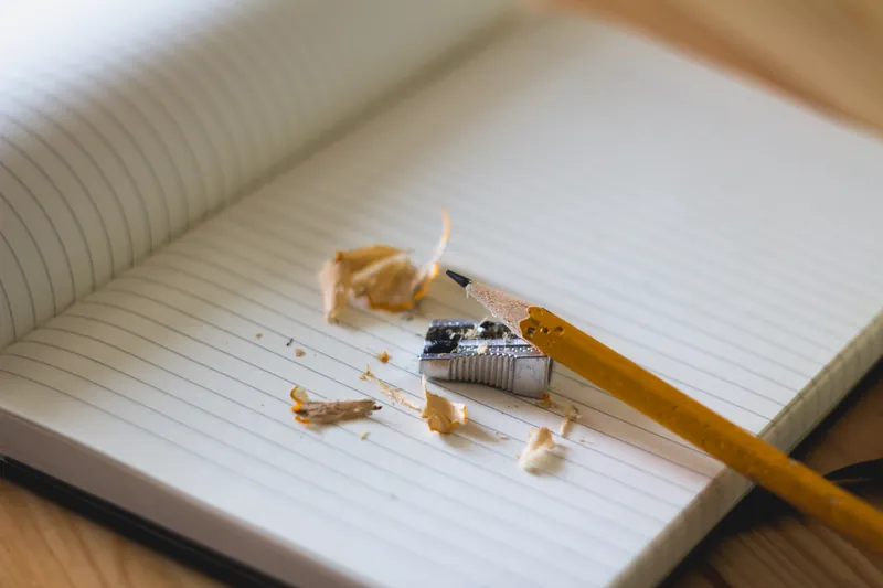 A sharpened pencil, a sharpener and wood shavings on an open ruled notebook.